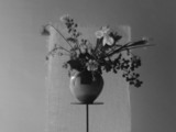 Black and white image of flowers in a vase on a tall stand