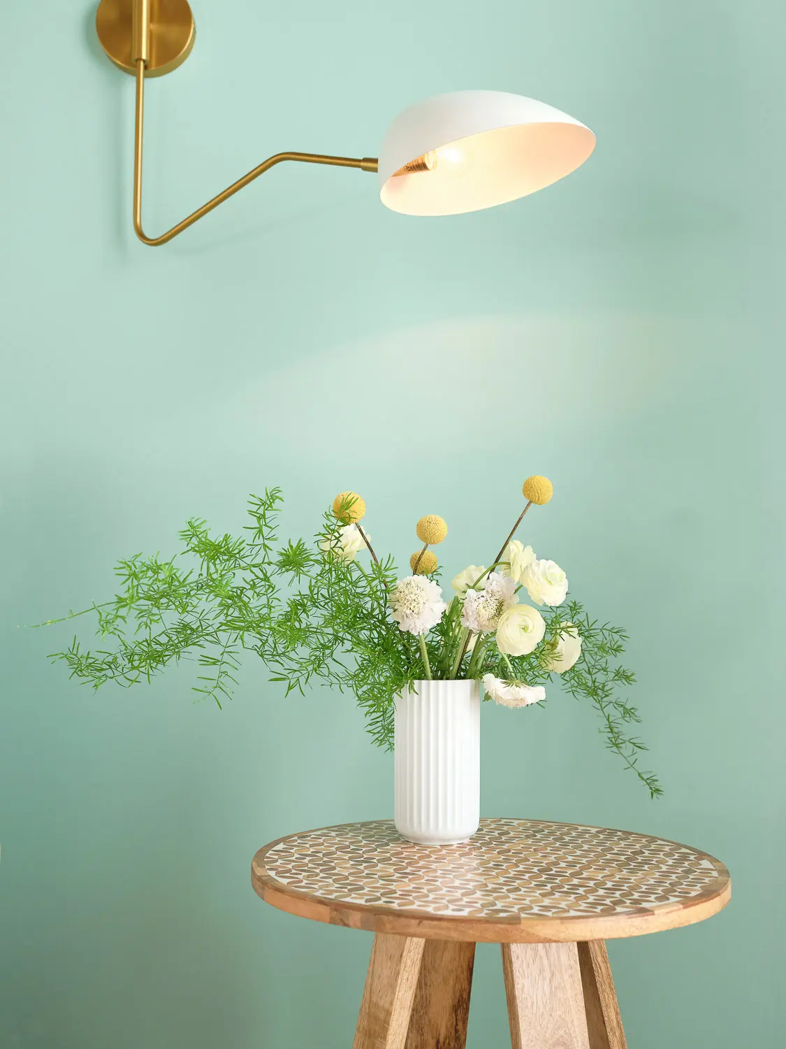 table with vase and flowers with a light above it