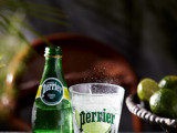 Commercial photograph of Perrier bottle with a glass, lime is in glass