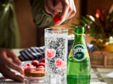 Commercial photograph of Perrier bottle with glass, bartender placing raspberry into glass