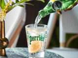 Commercial photograph of person pouring Perrier drink into glass, orange is in the glass